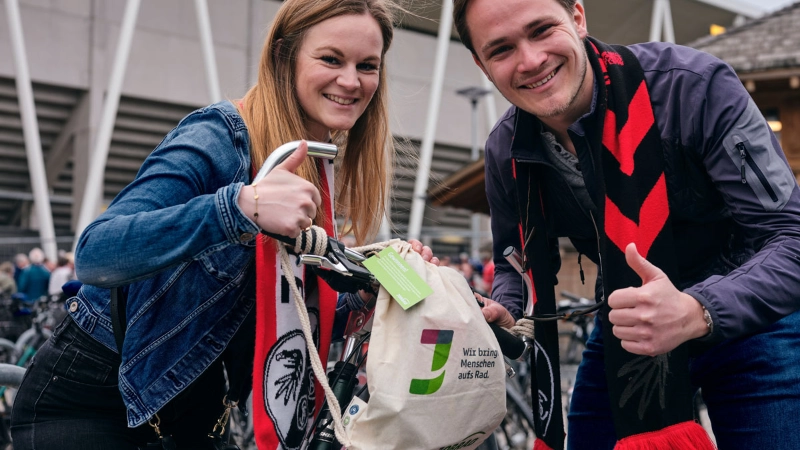 Ein Mann und eine Frau halten eine Goodie Bag am JobRad Aktionsspieltag Klimaschutz und machen beide die Daumen hoch Geste