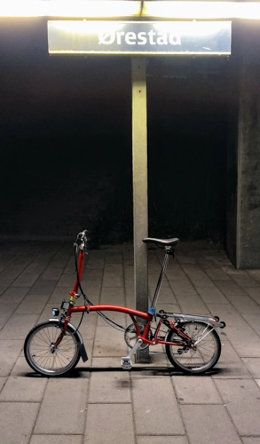 Ein rotes Faltrad an einem Bahnsteig mit dem Schild „Ørestad“.